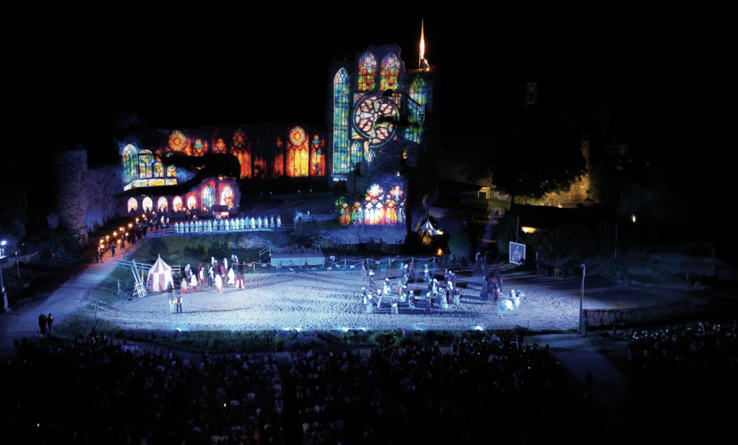 Un spectacle nocturne en plein air présenté dans le Talmont Saint-Hilaire Magazine met en scène des acteurs sur une scène éclairée, avec des vitraux illuminés de style gothique ressemblant à une cathédrale et un public nombreux. - Édition Offset 5 (Partenaire de votre communication locale en Vendée)