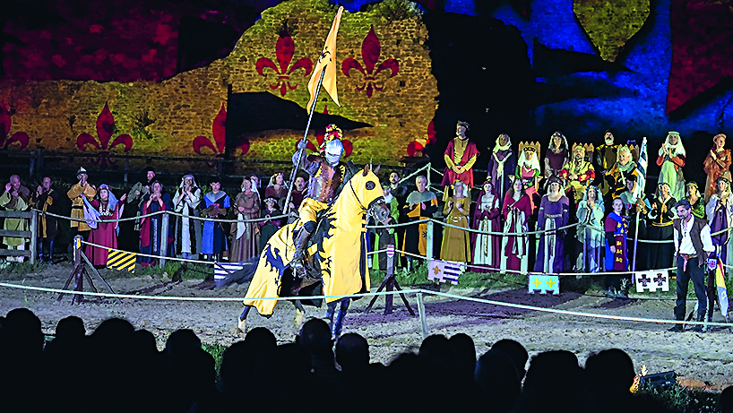 Un chevalier en armure jaune, tenant un drapeau, chevauche un cheval à tête jaune dans une arène. Derrière eux, des personnes en costumes médiévaux se tiennent devant une toile de fond à motifs de fleurs de lys. Au premier plan, un public observe la scène. - Édition Offset 5 (Partenaire de votre communication locale en Vendée)