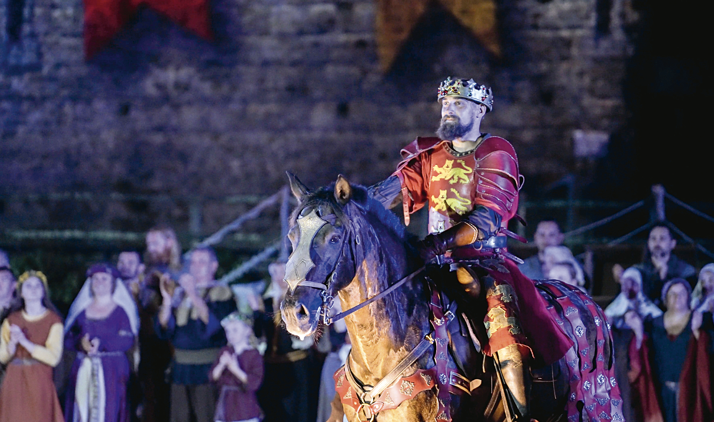 Un homme habillé comme un roi médiéval, portant une couronne et une robe rouge avec un emblème de lion, monte à cheval sous le regard de la foule - une scène emblématique présentée dans le Talmont Saint-Hilaire Magazine. - Édition Offset 5 (Partenaire de votre communication locale en Vendée)
