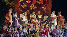 Un groupe de personnes vêtues de costumes médiévaux, notamment de couronnes et de robes, se réunit lors d'un événement en plein air présenté dans le magazine Talmont Saint-Hilaire, avec en arrière-plan un bâtiment ressemblant à un château magnifiquement illuminé. - Édition Offset 5 (Partenaire de votre communication locale en Vendée)