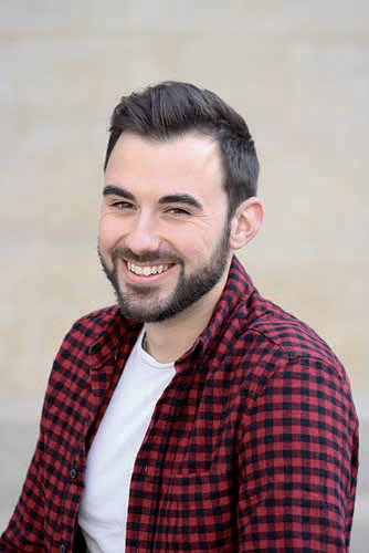 Un jeune homme aux cheveux bruns courts et à la barbe sourit. Il porte une chemise à carreaux rouges et noirs par-dessus un tee-shirt blanc et pose comme s'il était prêt pour un reportage dans le magazine Talmont Saint-Hilaire sur un fond uni de couleur claire. - Édition Offset 5 (Partenaire de votre communication locale en Vendée)