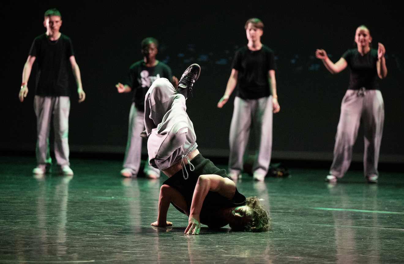 Un breakdancer se tient en équilibre sur une main, les jambes en l'air, sur la scène de l'Abbaye de Meslay, tandis que quatre personnes en chemise noire et pantalon gris regardent et applaudissent à l'arrière-plan. - Édition Offset 5 (Partenaire de votre communication locale en Vendée)