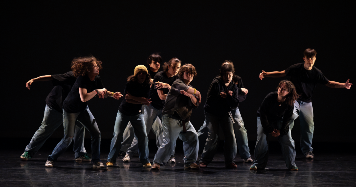 Un groupe de neuf personnes, dont Ruben Boisseleau, vêtues de hauts noirs et de jeans, exécutent une routine de danse dynamique sur scène, sur un fond sombre. Leurs poses et leurs expressions traduisent le mouvement et l'énergie. - Édition Offset 5 (Partenaire de votre communication locale en Vendée)