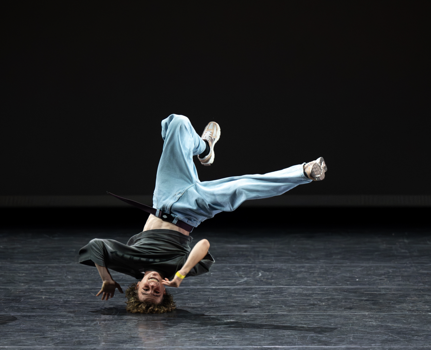 Un breakdancer vêtu d'un pantalon ample et de baskets se tient en équilibre sur la tête, les jambes tendues dans les airs, exécutant un mouvement dynamique sur scène, sur un fond sombre - une démonstration impressionnante de Ruben Boisseleau. - Édition Offset 5 (Partenaire de votre communication locale en Vendée)