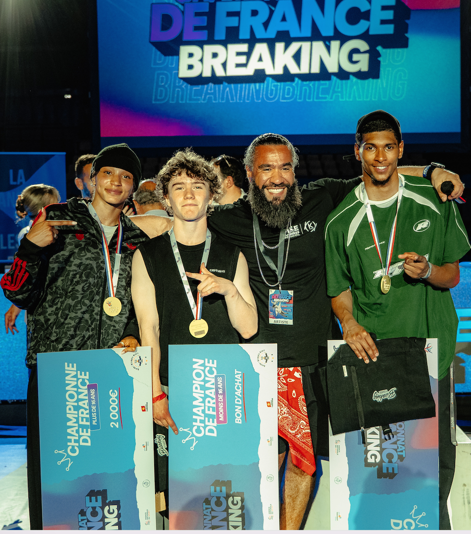 Quatre hommes, dont Ruben Boisseleau, posent et sourient pour une photo de célébration lors d'une compétition de breakdance, portant des médailles et tenant des certificats de champion, avec derrière eux une toile de fond colorée de la rupture du Champion de France. - Édition Offset 5 (Partenaire de votre communication locale en Vendée)