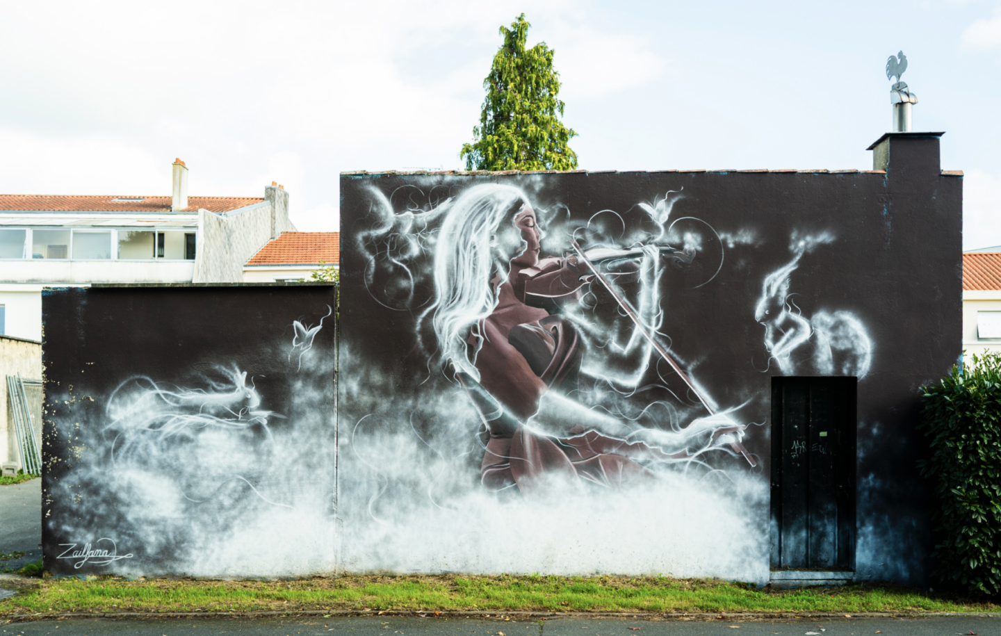 Une peinture murale de Simon Boisliveau sur un mur noir représente une femme jouant du violon, entourée de volutes de fumée blanche formant des animaux fantomatiques ; des arbres et des bâtiments émergent subtilement à l'arrière-plan. - Édition Offset 5 (Partenaire de votre communication locale en Vendée)