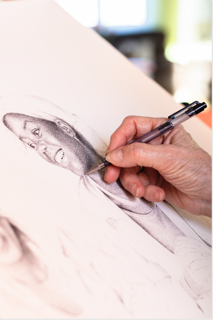 Gros plan d'une main dessinant un portrait détaillé d'une femme à la plume sur du papier blanc au Manoir de la Mortière. L'artiste a ombré la zone du cou, et le portrait inachevé montre le visage et la partie supérieure du torse de la femme. - Édition Offset 5 (Partenaire de votre communication locale en Vendée)