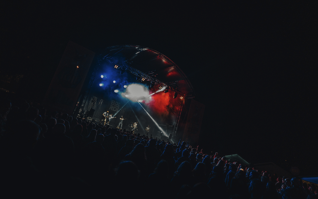 Une foule regarde Ruben Boisseleau et son groupe se produire sur une scène en plein air, la nuit, éclairée par des lumières colorées rouges, bleues et blanches dans un ciel sombre. - Édition Offset 5 (Partenaire de votre communication locale en Vendée)