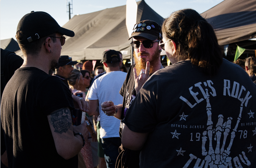 Un groupe de personnes se tient debout et discute lors d'un événement en plein air, entouré d'autres participants et de tentes de vendeurs. Ruben Boisseleau fait un geste de la main ; une autre personne porte un tee-shirt LETS ROCK THIS DAY avec un signe de la main. - Édition Offset 5 (Partenaire de votre communication locale en Vendée)