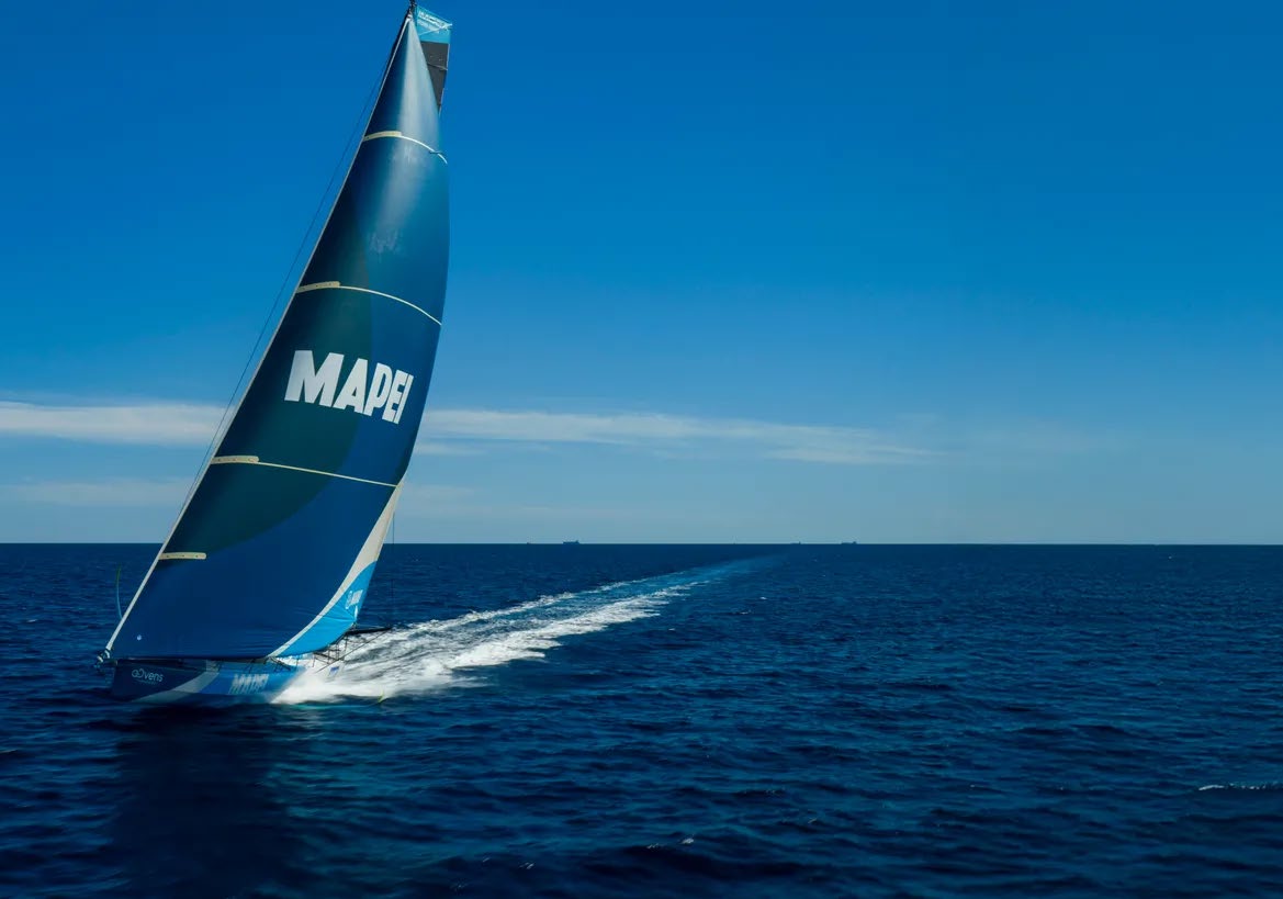 Un voilier bleu et blanc portant l'inscription MAPEI sur sa voile et gréé de deux grand-voiles et de quatre cornes glisse rapidement sur l'océan, laissant derrière lui une longue traînée blanche sous un ciel bleu limpide. - Édition Offset 5 (Partenaire de votre communication locale en Vendée)