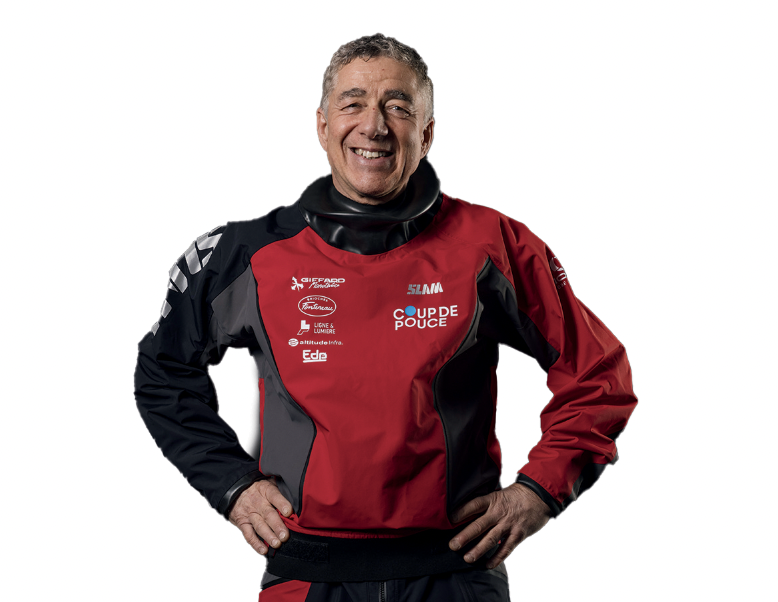 Un homme souriant se tient debout, les mains sur les hanches, vêtu d'une veste de voile imperméable rouge et noire arborant divers logos de sponsors, dont 2 Mains 4 Cornes. L'arrière-plan est blanc. - Édition Offset 5 (Partenaire de votre communication locale en Vendée)