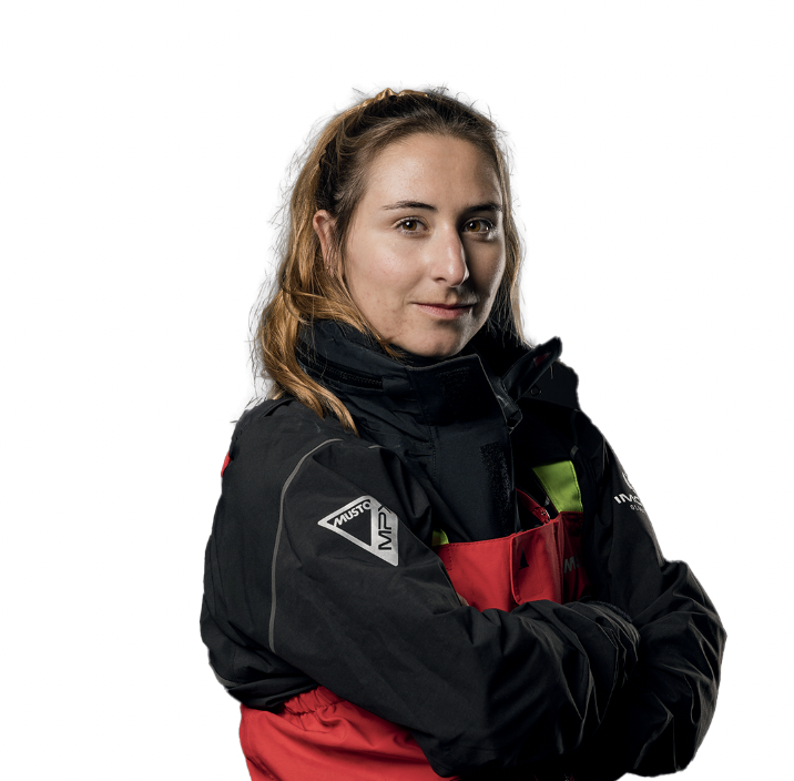 Une femme aux longs cheveux bruns portant une veste d'extérieur rouge et noire 2 Mains 4 Cornes se tient debout, les bras croisés, regardant l'appareil photo avec assurance sur un fond blanc. - Édition Offset 5 (Partenaire de votre communication locale en Vendée)