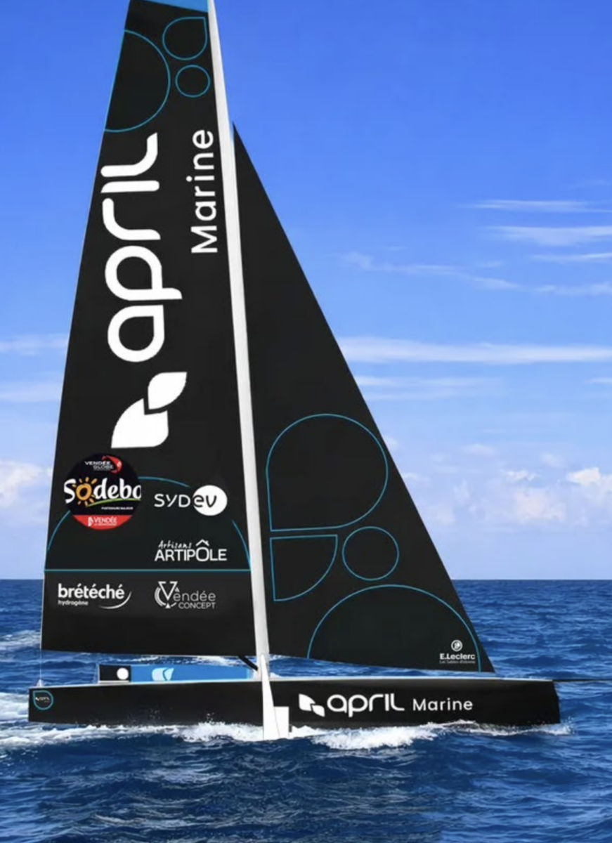 Un élégant voilier noir portant la marque April Marine et l'insigne "2 Mains 4 Cornes" navigue sur l'eau bleue de l'océan sous un ciel clair et lumineux. La voile du bateau comporte plusieurs logos de sponsors et des motifs géométriques bleus saisissants. - Édition Offset 5 (Partenaire de votre communication locale en Vendée)
