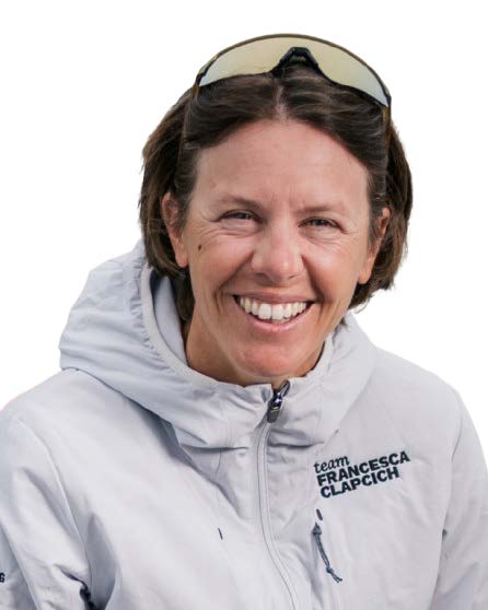 Une femme aux cheveux bruns courts, portant des lunettes de soleil sur la tête et une veste gris clair 2 Mains 4 Cornes sur laquelle on peut lire Team Francesca Clapcich, sourit à la caméra sur un fond blanc. - Édition Offset 5 (Partenaire de votre communication locale en Vendée)