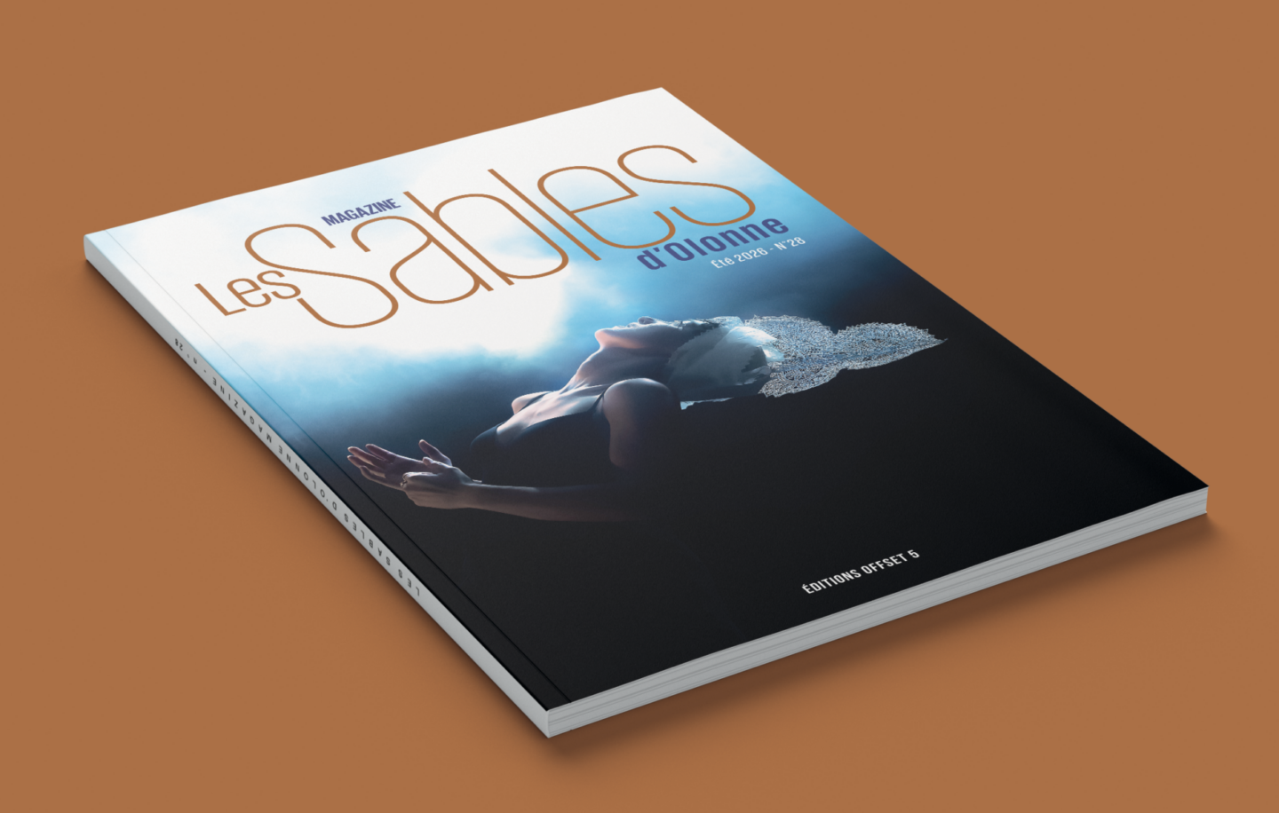 Un magazine intitulé Les Sables d'Olonne est posé sur une surface brune, avec en couverture l'image spectaculaire d'une femme de profil, la tête penchée en arrière sous une lumière douce, portant une coiffe décorative étincelante - l'inspiration parfaite après avoir exploré le Bike Park Montaigu-Vendée. - Édition Offset 5 (Partenaire de votre communication locale en Vendée)