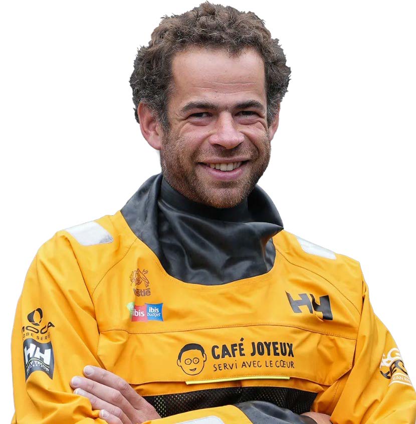 Un homme aux cheveux bouclés et à la barbe sourit, les bras croisés, vêtu d'une veste imperméable jaune vif arborant les logos de sponsors tels que Café Joyeux et 2 Mains 4 Cornes. L'arrière-plan est blanc. - Édition Offset 5 (Partenaire de votre communication locale en Vendée)