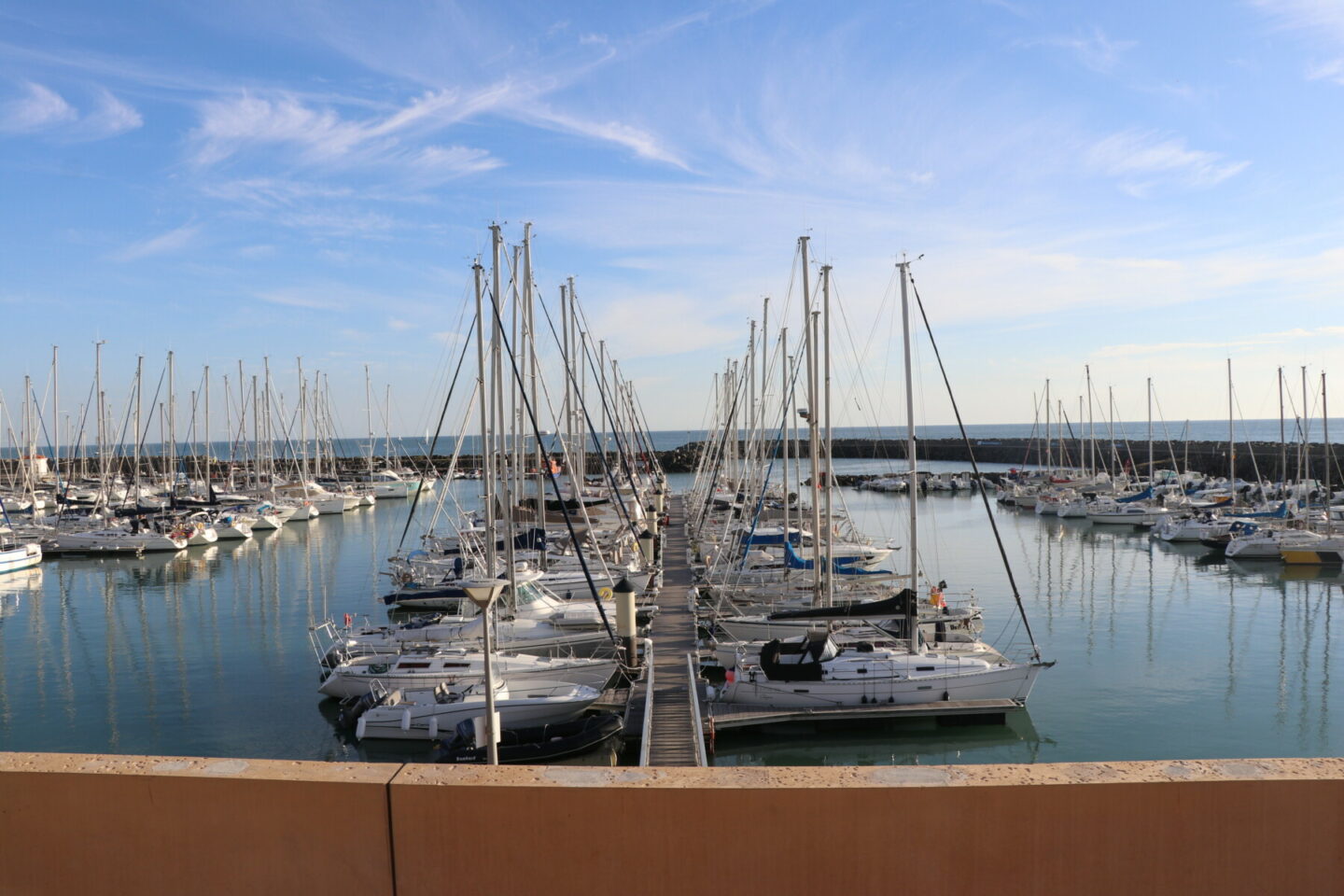 Une marina où s'alignent voiliers et yachts amarrés, des eaux calmes dans lesquelles se reflètent les bateaux, et un ciel bleu parsemé de nuages vaporeux : tout cela compose un spectacle d'une beauté sereine. - Édition Offset 5 (Partenaire de votre communication locale en Vendée)
